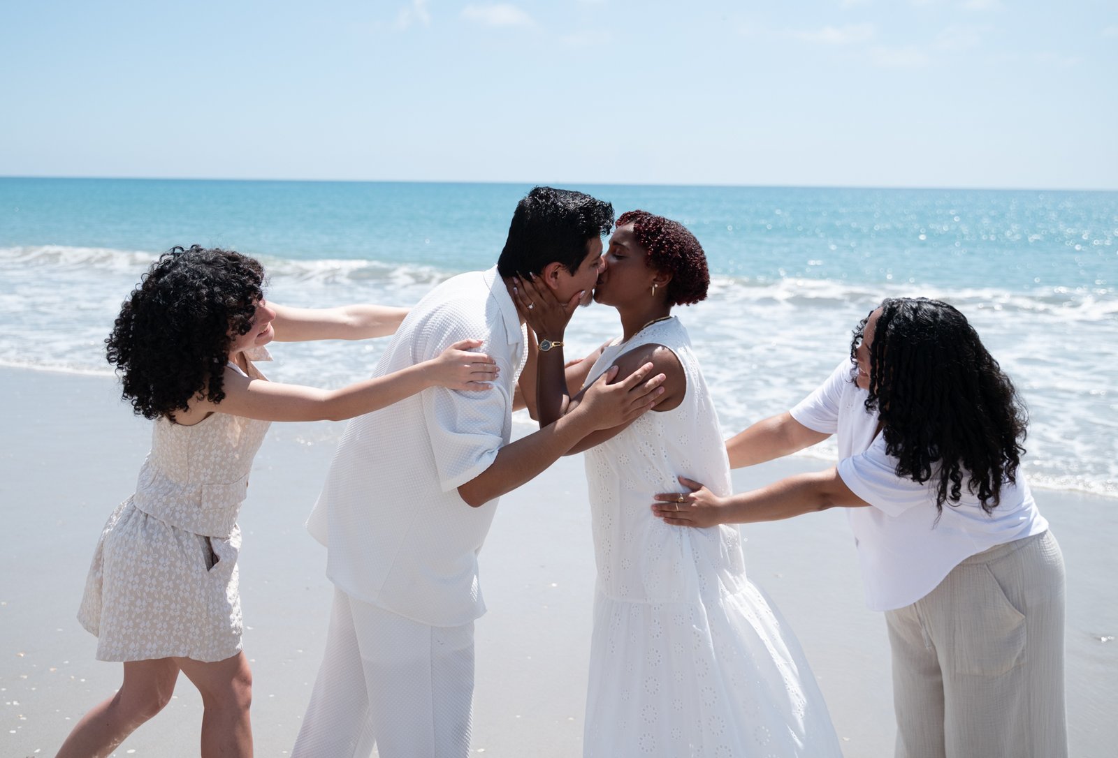 Josue and Yassiel kissing on the beach, surrounded by loved ones